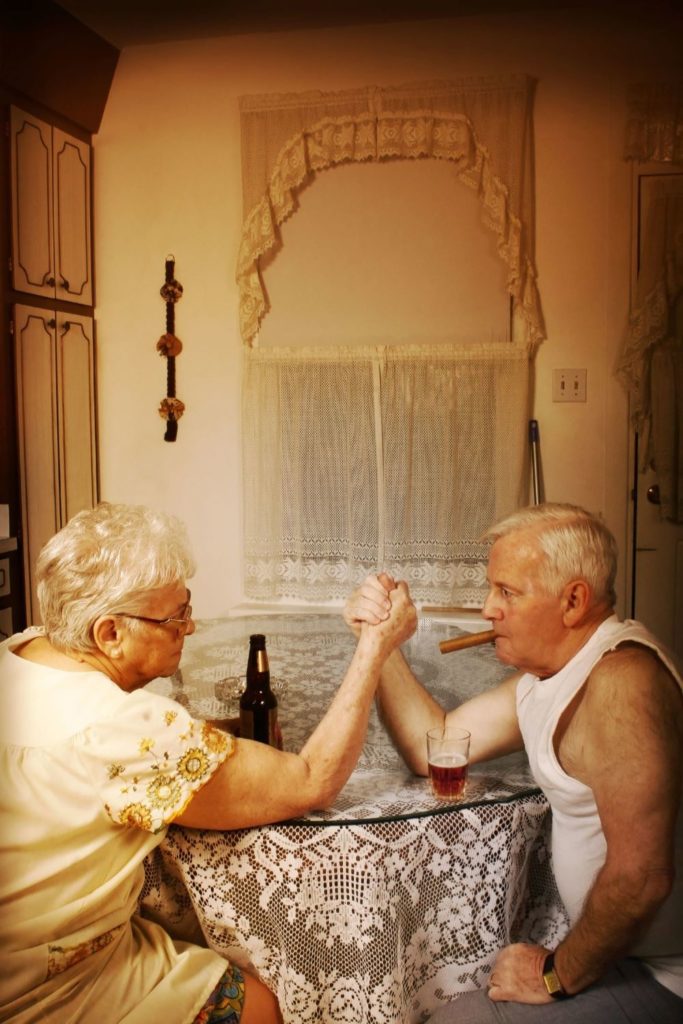 alt text = "senior couple with drinks arm wrestles"