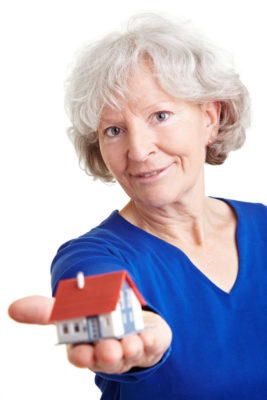 alt="Female senior citizen offers model of single family home to potential buyers"
