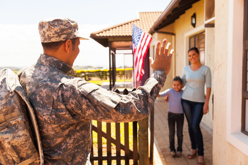 alt="Soldier greeting family on front porch of the home he financed with a VA home loan"