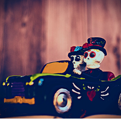 alt text = "day of the dead skeleton couple with hats on drive a car to enjoy some fun october events"