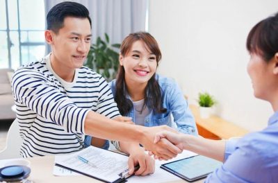 alt text = young couple sitting across from a mortgage broker excited for their preapproval the man and broker shake hands"