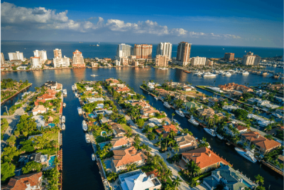 alt="Aerial view of canal and intracoastal front single family homes with oceanfront condos in the background."