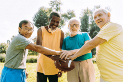 alt = "a group of four four older men huddle around a football in may 2022 in south florida"